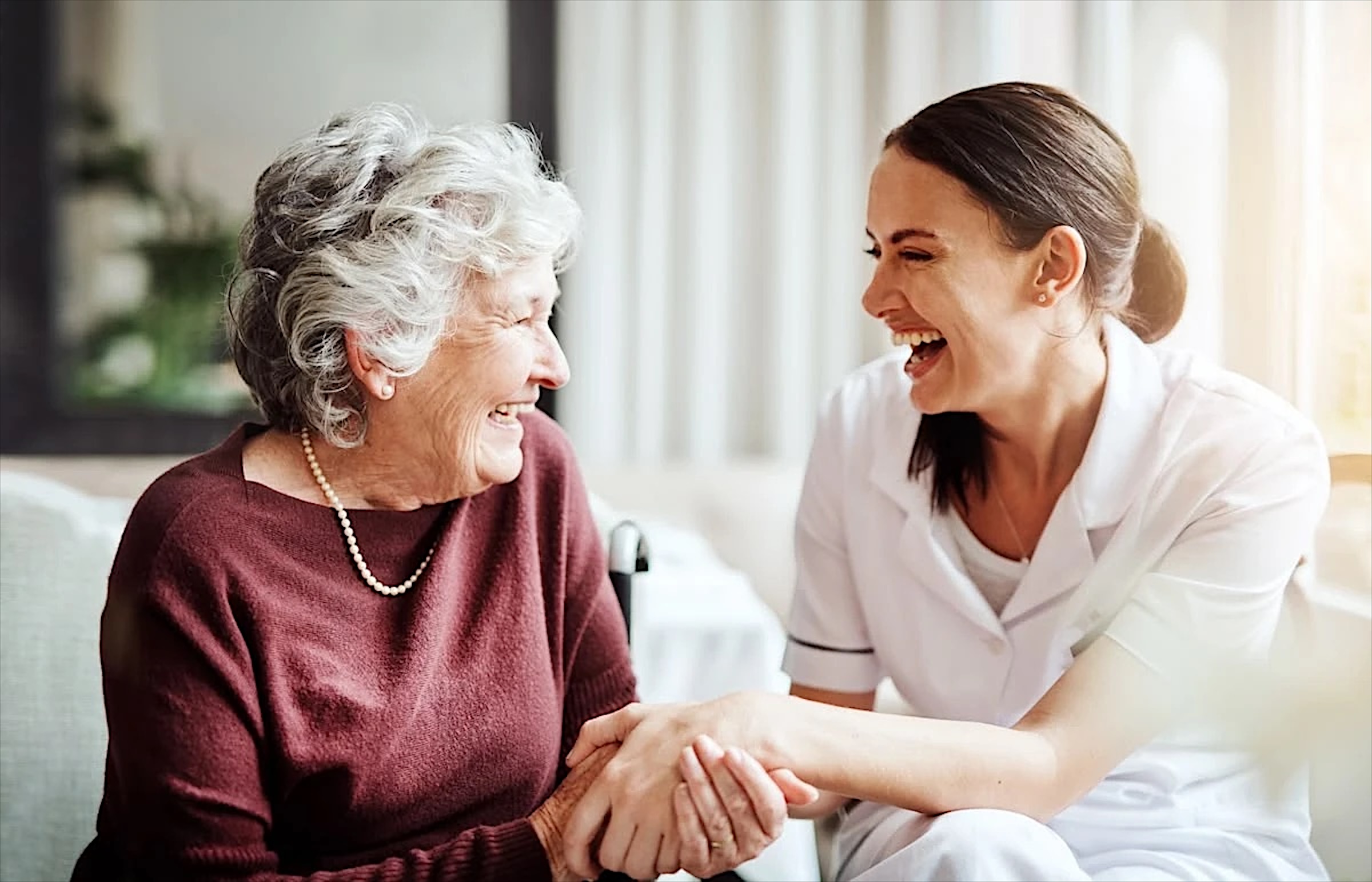 A carer and an older woman laughing together, holding hands