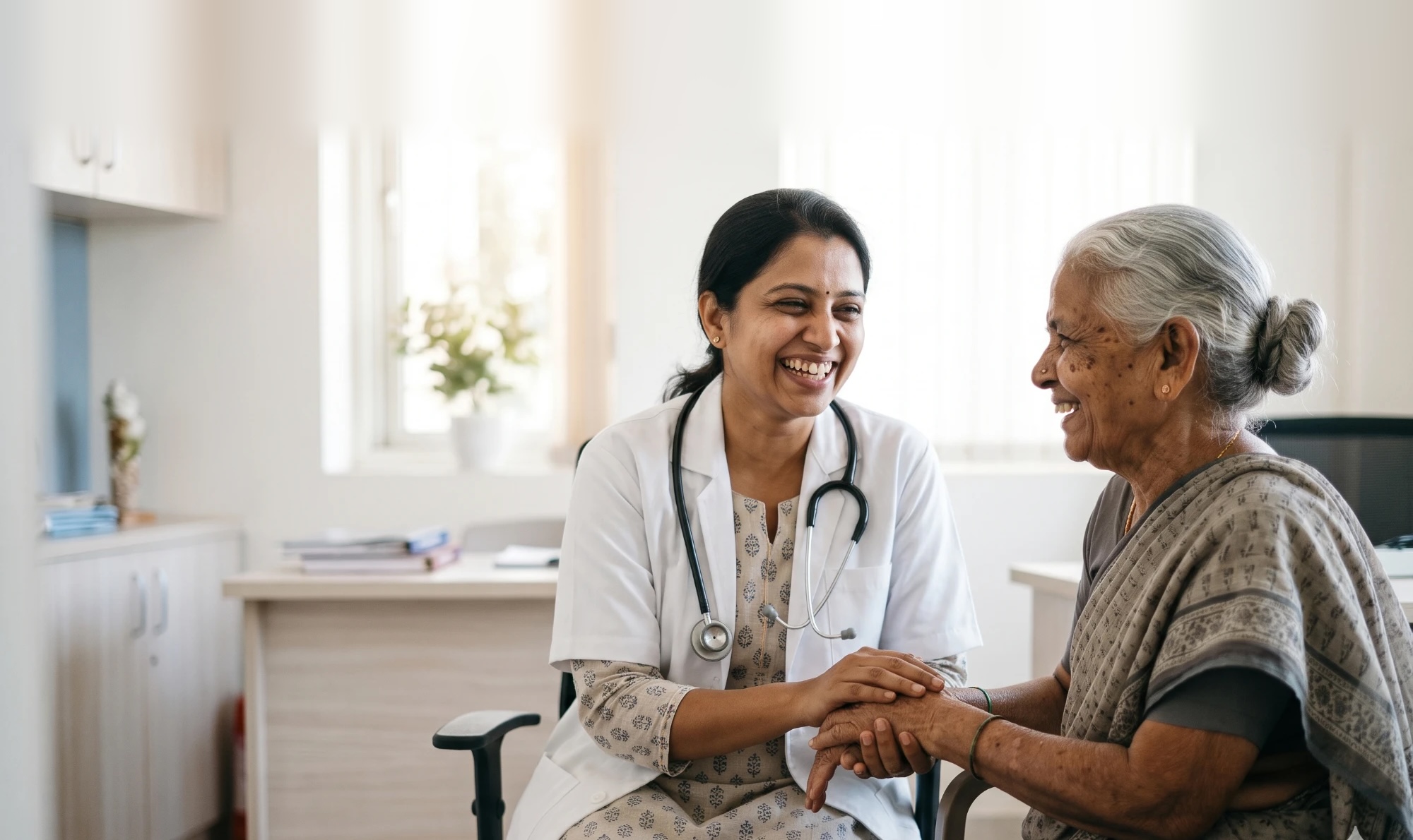 A doctor laughing with an older patient, holding her hands